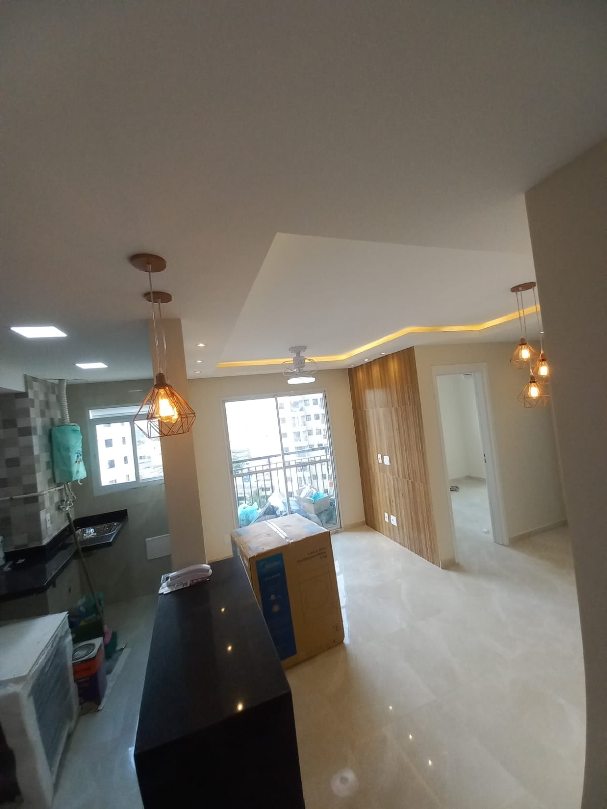 Sala integrada com cozinha, iluminação e painel de madeira